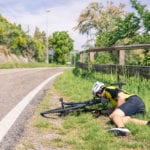 Male cyclist lying in the grass on the side of the road after falling off his bicycle.