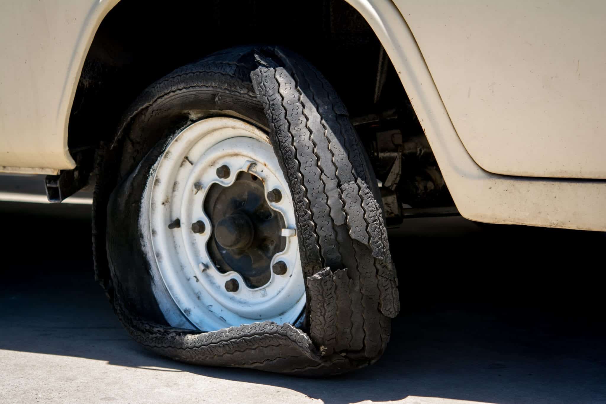 A close-up of a wheel on a a white vehicle with a badly destroyed tire.