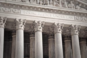 A close-up of the top of a large neoclassical courthouse building with several corinthian style columns and the words EQUAL JUSTICE UNDER LAW engraved on the front of the building above the columns.