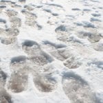 Footprints in the snow on and icy walkway.