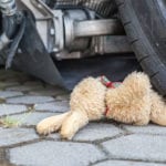 A close-up of a car tire running over the legs of a child's brown stuffed animal.