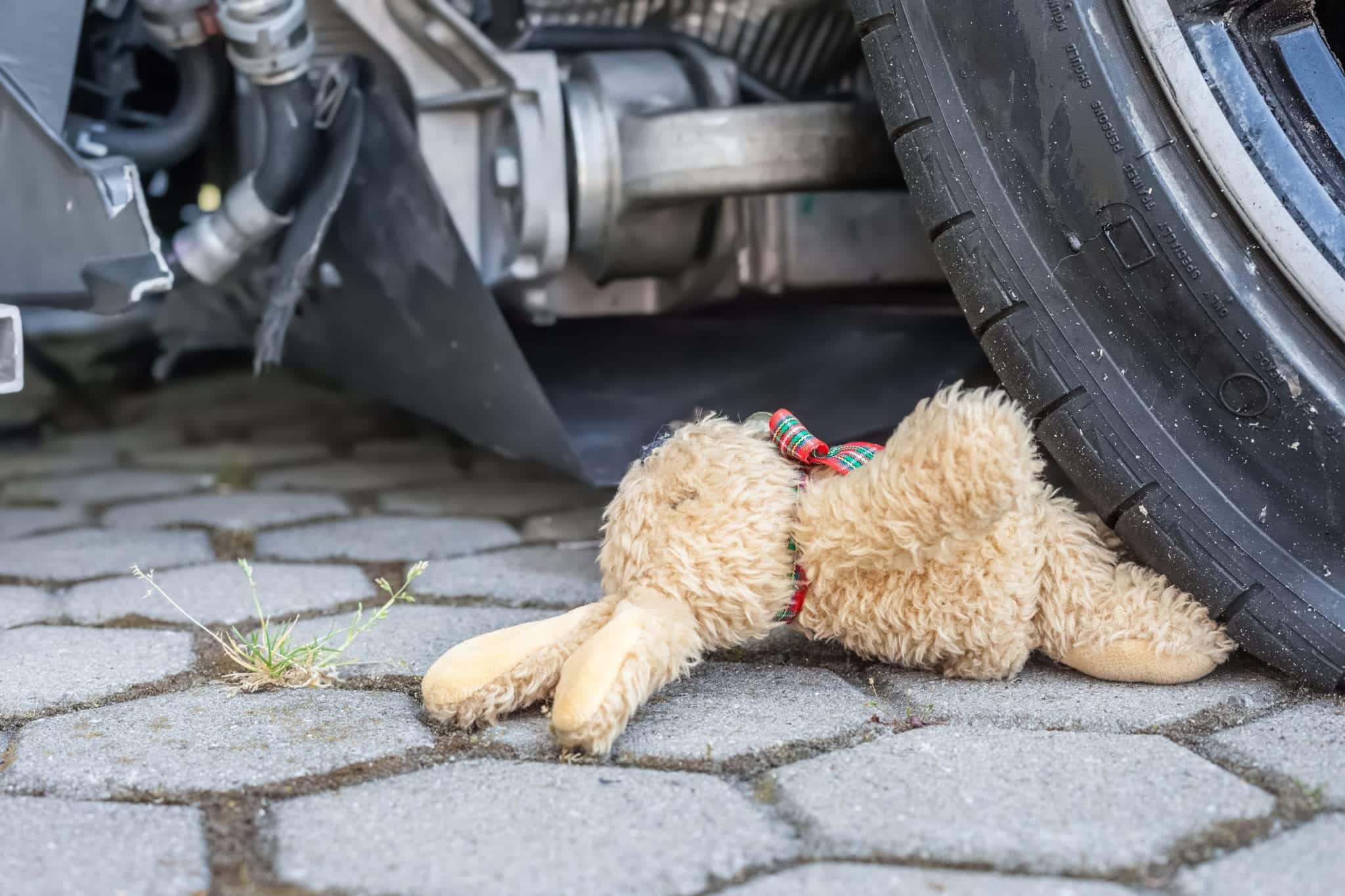 A close-up of a car tire running over the legs of a child's brown stuffed animal.