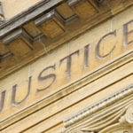 The word JUSTICE engraved on the front of a stone government building with a classic architectural design.