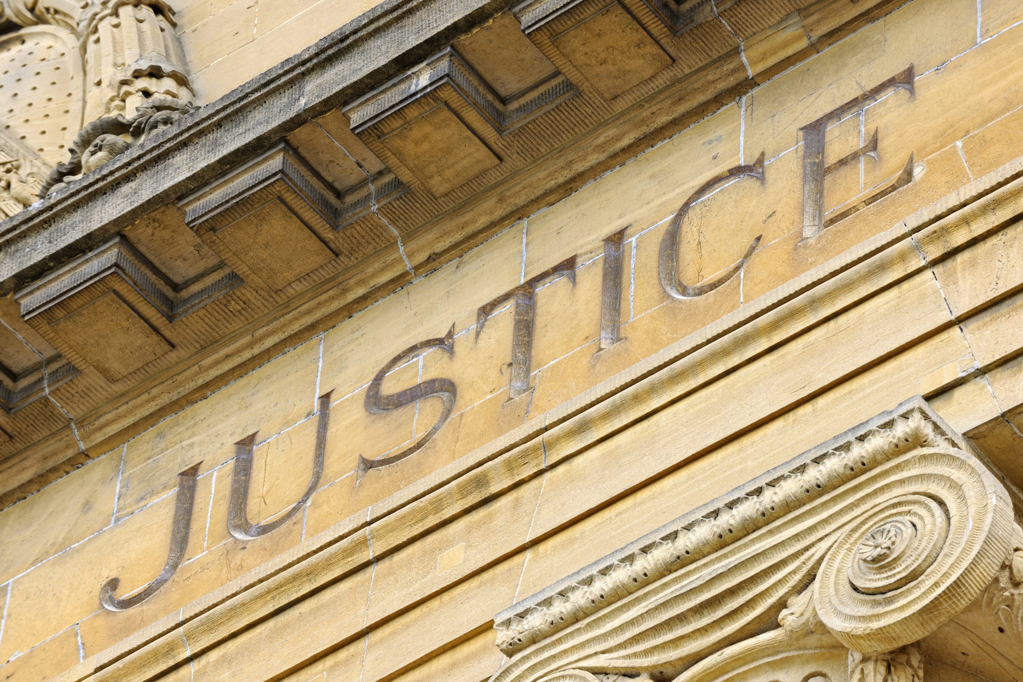 The word JUSTICE engraved on the front of a stone government building with a classic architectural design.