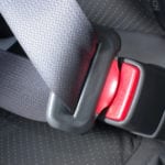 A close up of a buckled gray seatbelt with a red button that says PRESS.