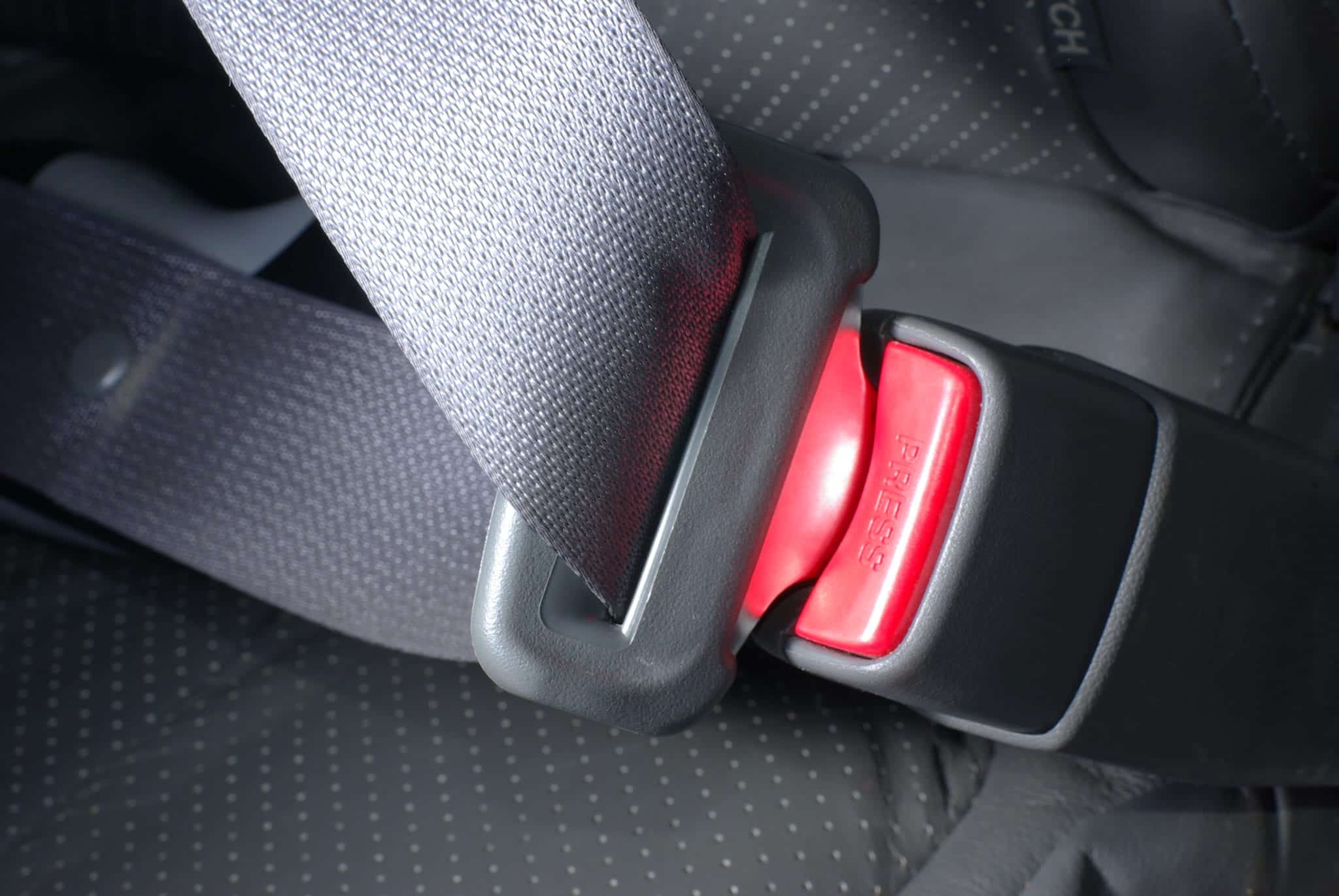 A close up of a buckled gray seatbelt with a red button that says PRESS.