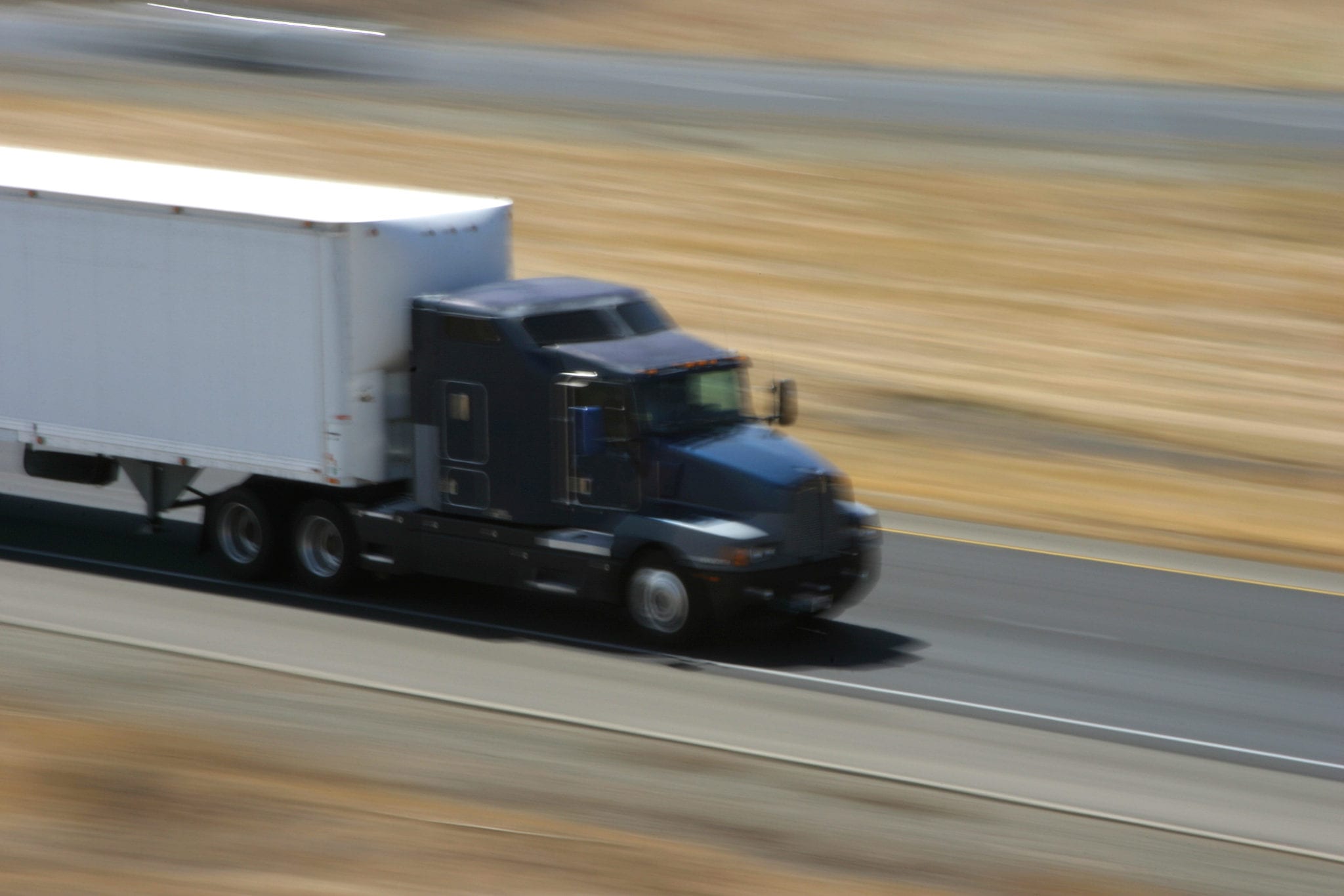 A blurry view of a tractor trailer traveling on the highway, appearing to be traveling at a high speed.