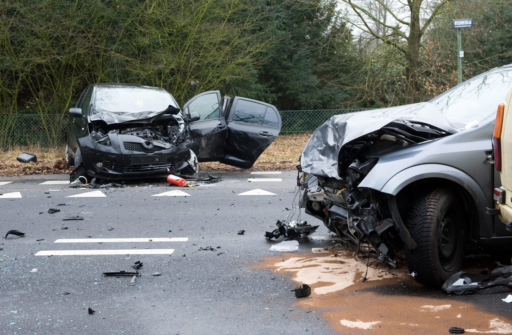 A black car and a grey car in a wreck scene on a a road with their front ends completely smashed in, appearing to have had a bad front end collision.