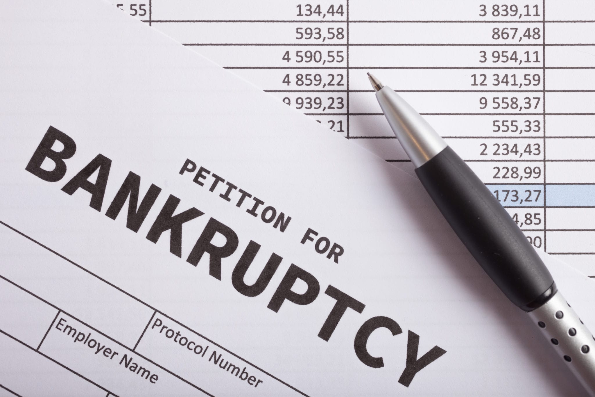 A ballpoint pen laying on financial documents with the words PETITION FOR BANKRUPTCY at the top.