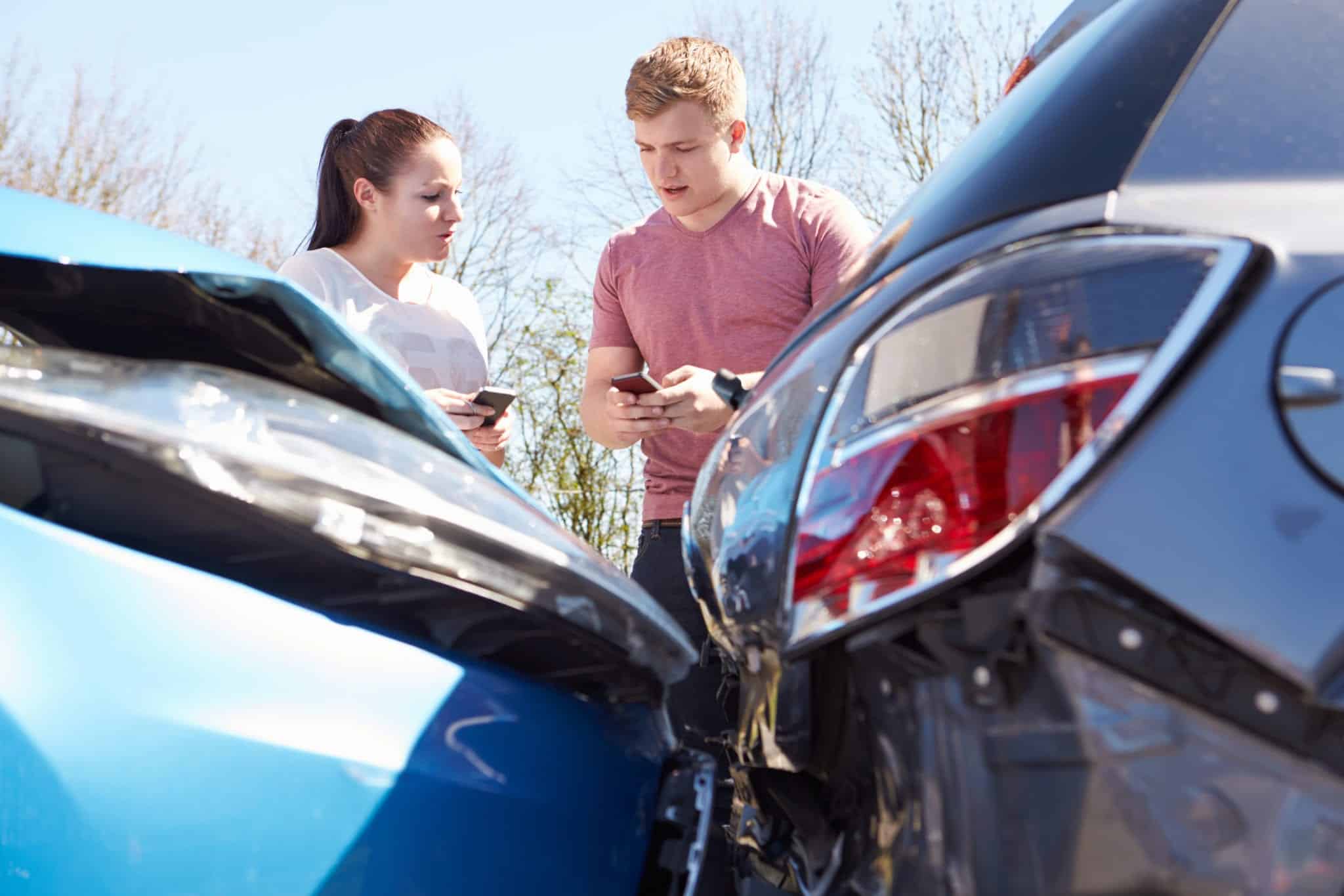 The foreground shows a blue car hitting the back of a black car with a woman and a man standing in the background holding their phones.