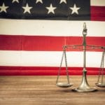 The scales of justice sitting on a wooden table with an american flag background.