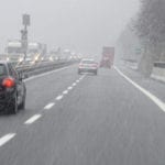 View from the windshield of a car driving on a two lane highway, following other cars, during a snowstorm.