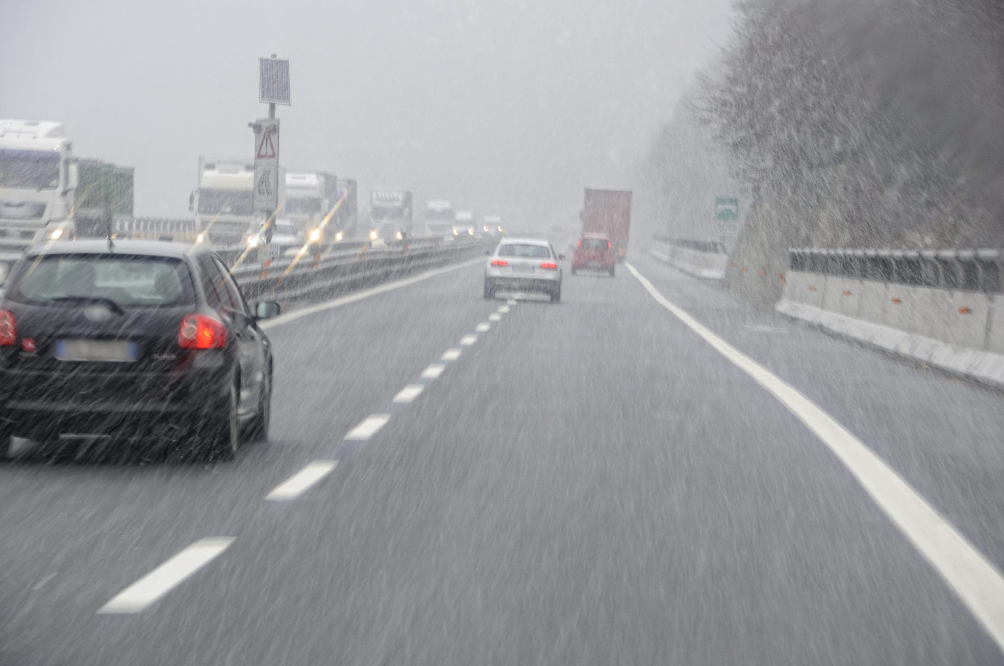 View from the windshield of a car driving on a two lane highway, following other cars, during a snowstorm.