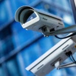 Two white security cameras against a blurred background of a building.