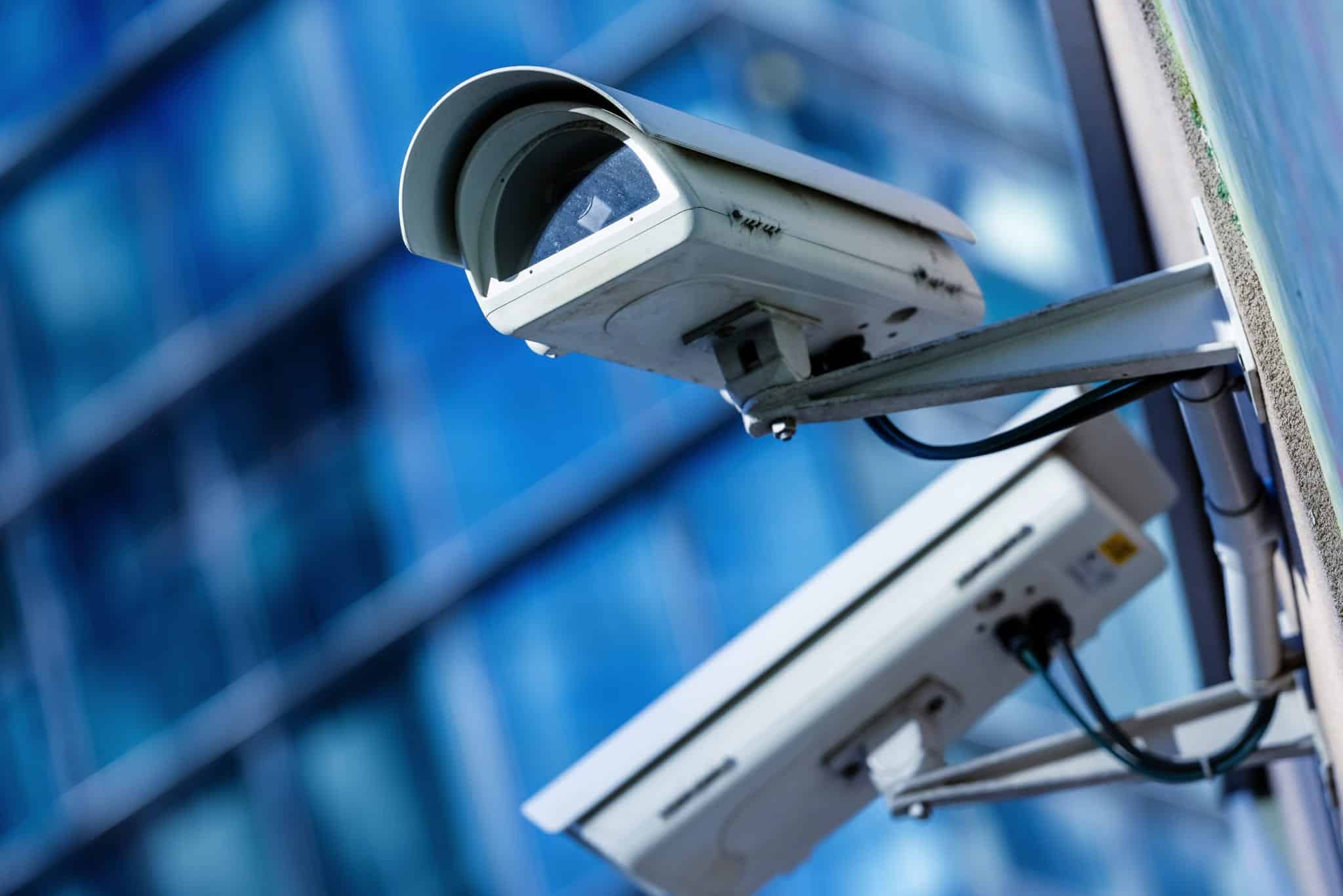 Two white security cameras against a blurred background of a building.