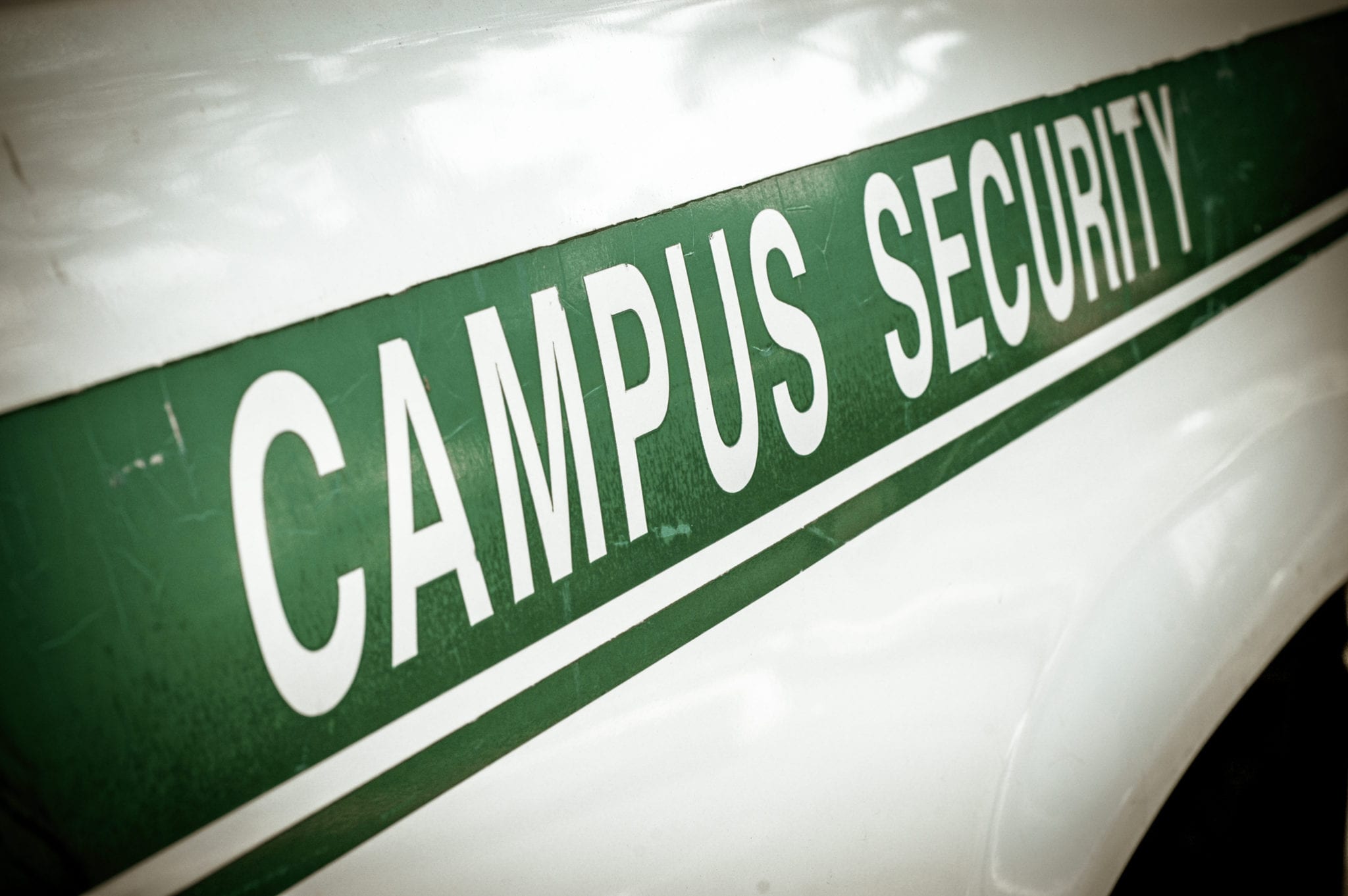 A close-up of the side of a white car with a diagonal green strip with the words CAMPUS SECURITY.