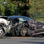 Two severely damaged cars with their front ends completely smashed in, still on the road where they collided.