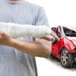 Injured person with cast on arm standing in front of a severely damaged red car.