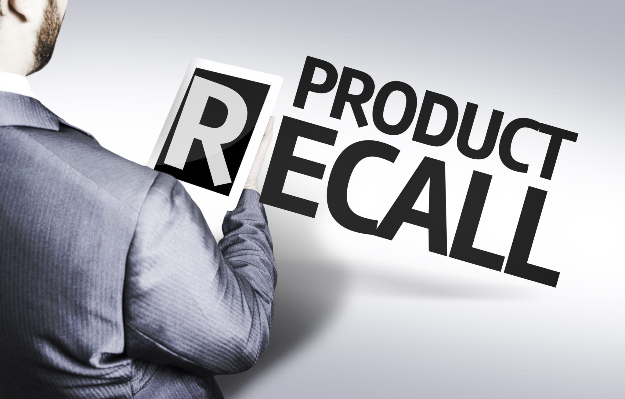 Looking over the shoulder of a man in a business suit at the words Product Recall.