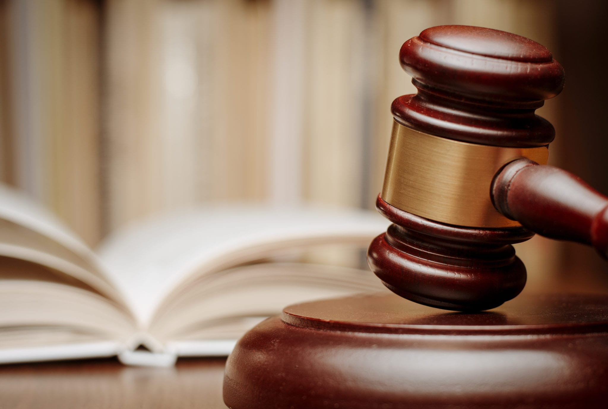 A closeup of a wooden gavel with a blurred background of a white open book.