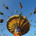 A view looking up at people riding on amusement park swings with a clear blue sky above them.