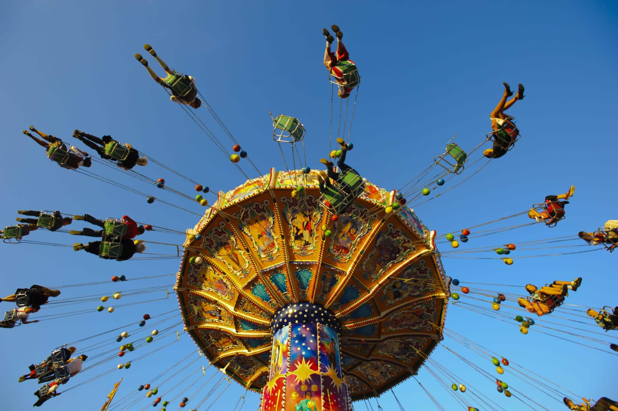 A view looking up at people riding on amusement park swings with a clear blue sky above them.