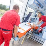 Two paramedics loading a patient, straped to a gurney, into an ambulance.