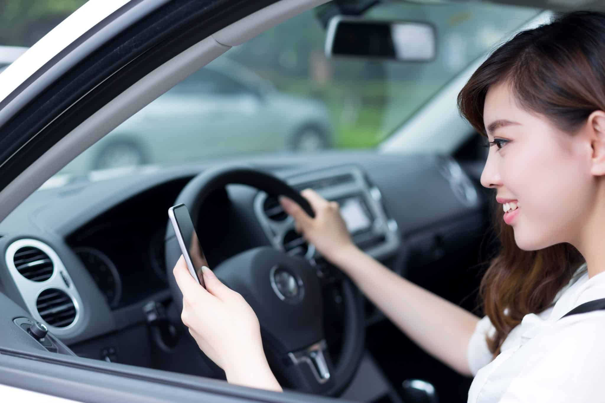 A woman texting on a cellphone with her left hand while she steers a car with her right hand.