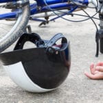 A blue bike and a black and white bike helmet laying on concrete with someone's hand resting on the ground, the person's body is out of the frame and cannot be seen.