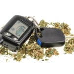 A black car key and key fob surrounded by dried marijuana leaves on a white background.