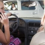 Two teens driving in a car, the driver on the phone not paying attention to the car infront of her that shes about to run into.