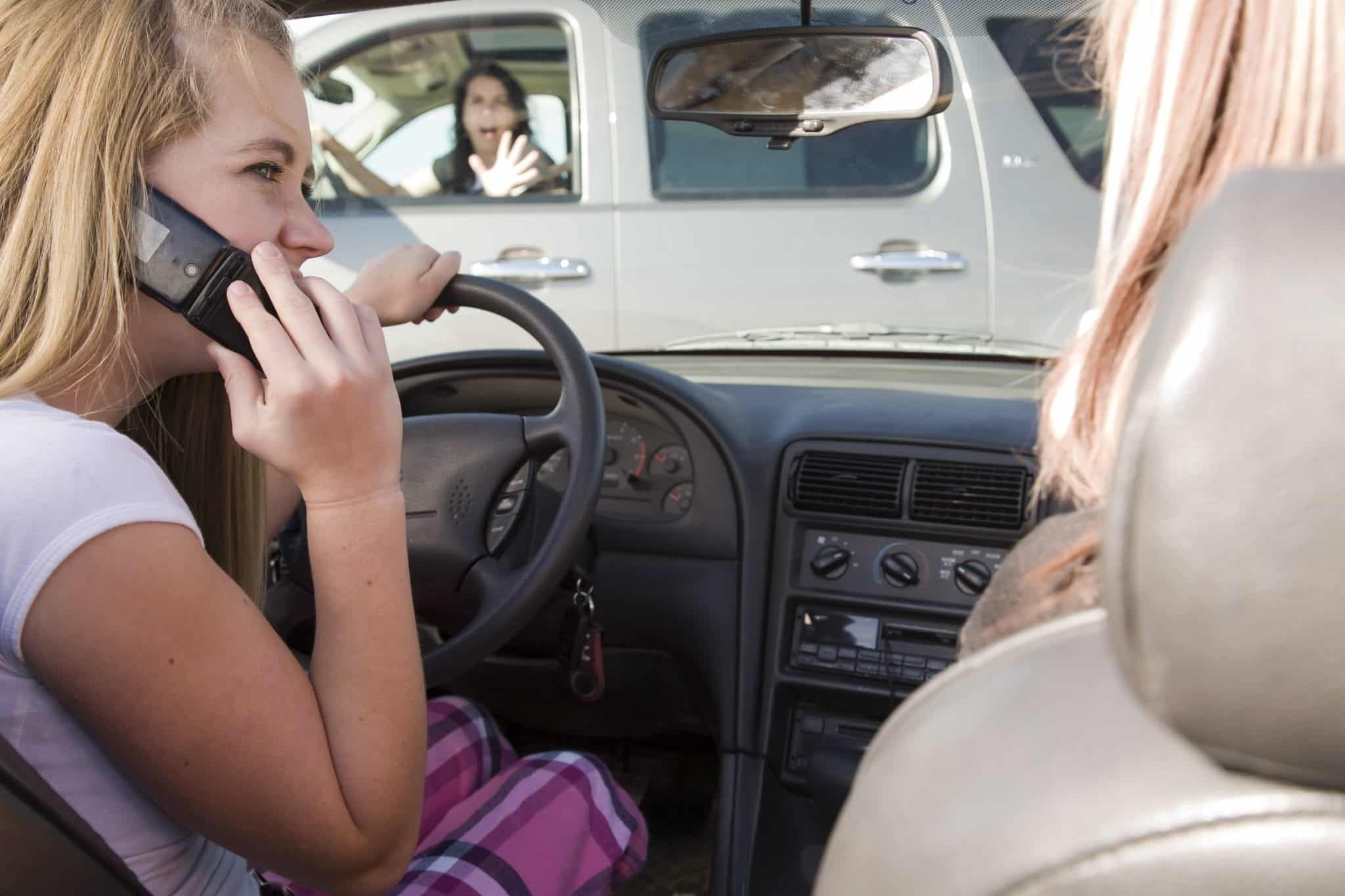 Two teens driving in a car, the driver on the phone not paying attention to the car infront of her that shes about to run into.