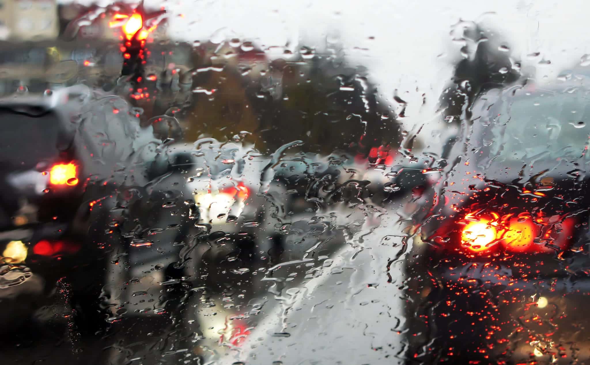 Looking through a car windshield covered in rain drops, obscuring the view of the surrounding bumper to bumper traffic.