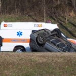 The bottom of a gray SUV having rolled over during a wreck with an ambulance in the background.