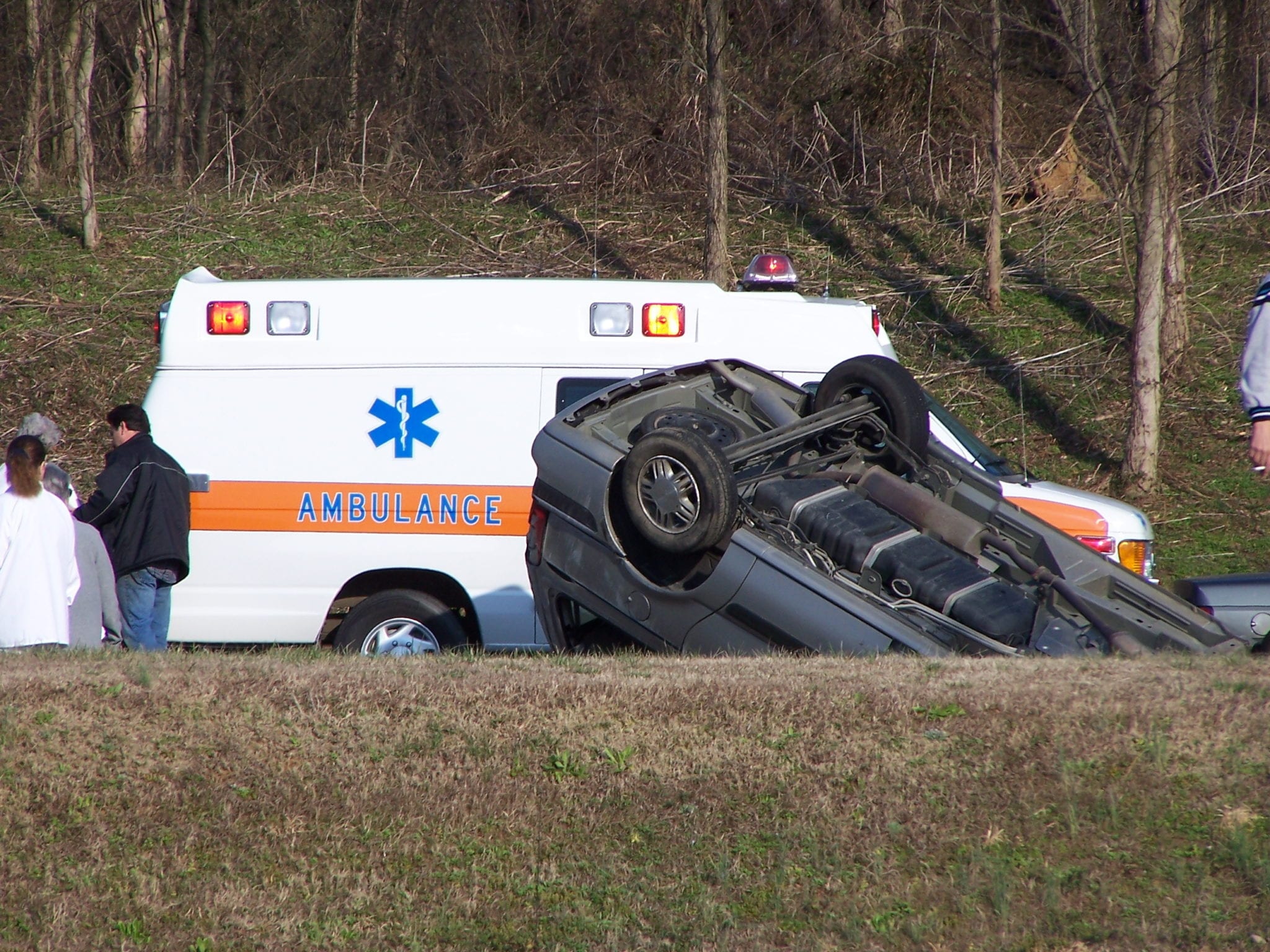 The bottom of a gray SUV having rolled over during a wreck with an ambulance in the background.