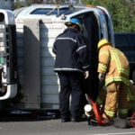 Two firefighters tending to a wreck scene with a white tractor trailer on it's side.