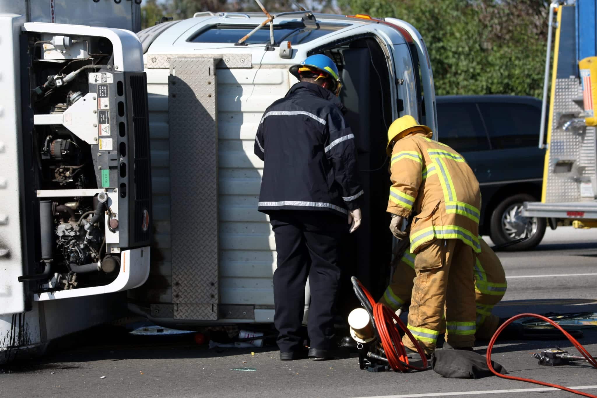 Two firefighters tending to a wreck scene with a white tractor trailer on it's side.