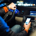 A man on his phone while driving in his car at night.