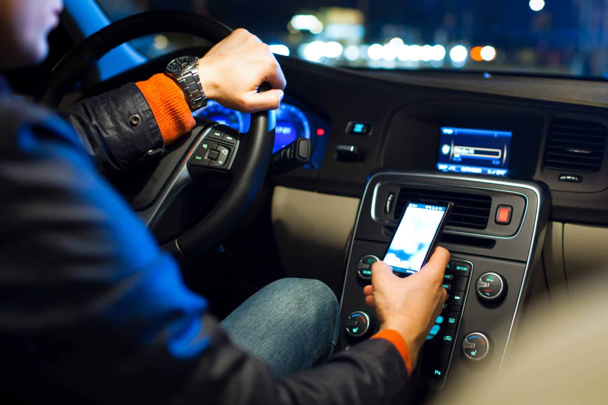 A man on his phone while driving in his car at night.