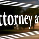 A black sign with the words Attorney at Law in white letters and a blurry scene of an outdoor setting reflecting off of the black sign.