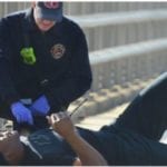 A paramedic wearing purple gloves, tending to a man lying on the ground.