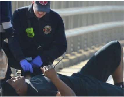 A paramedic wearing purple gloves, tending to a man lying on the ground.