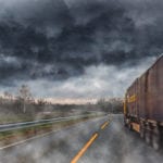 The back of a tractor trailer driving down a road during a bad rainstorm.