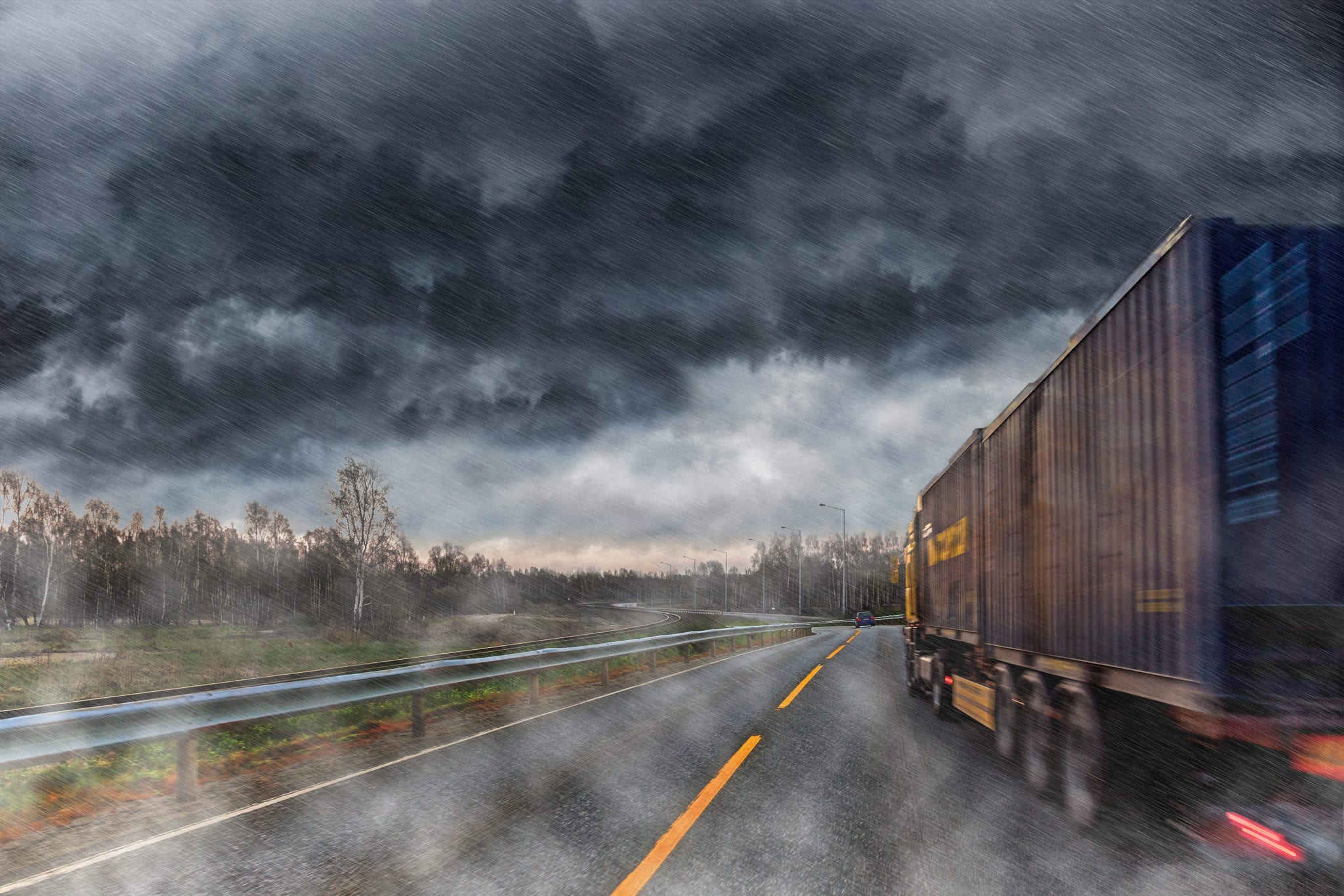 The back of a tractor trailer driving down a road during a bad rainstorm.