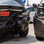 Two severely damaged cars, the back of a black car smashed in and the front of a gray car smashed in.