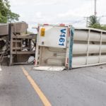 A tractor trailer flipped on its side laying accross the road.