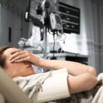 A woman laying in a hospital bed with her hand covering her eyes.