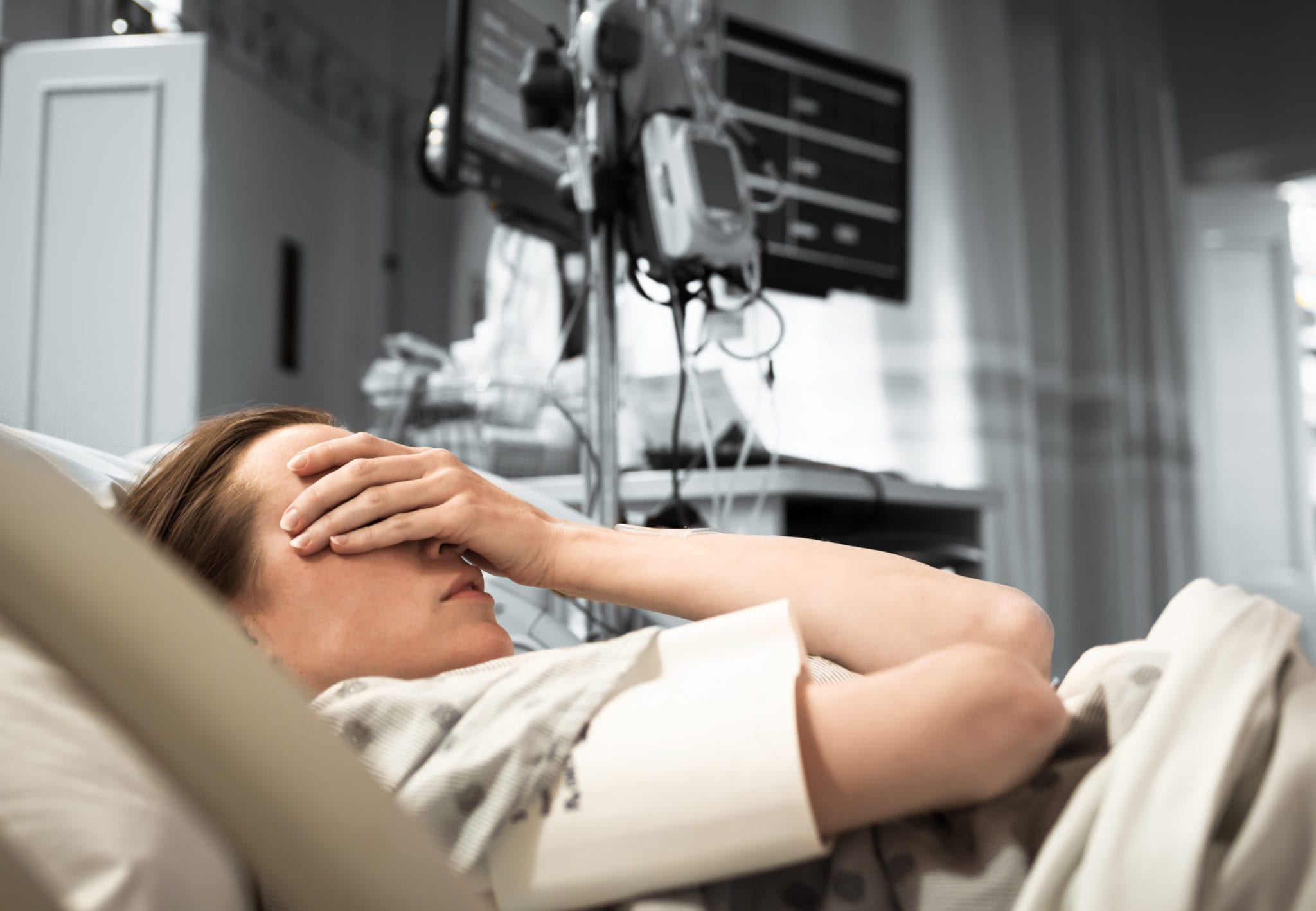 A woman laying in a hospital bed with her hand covering her eyes.