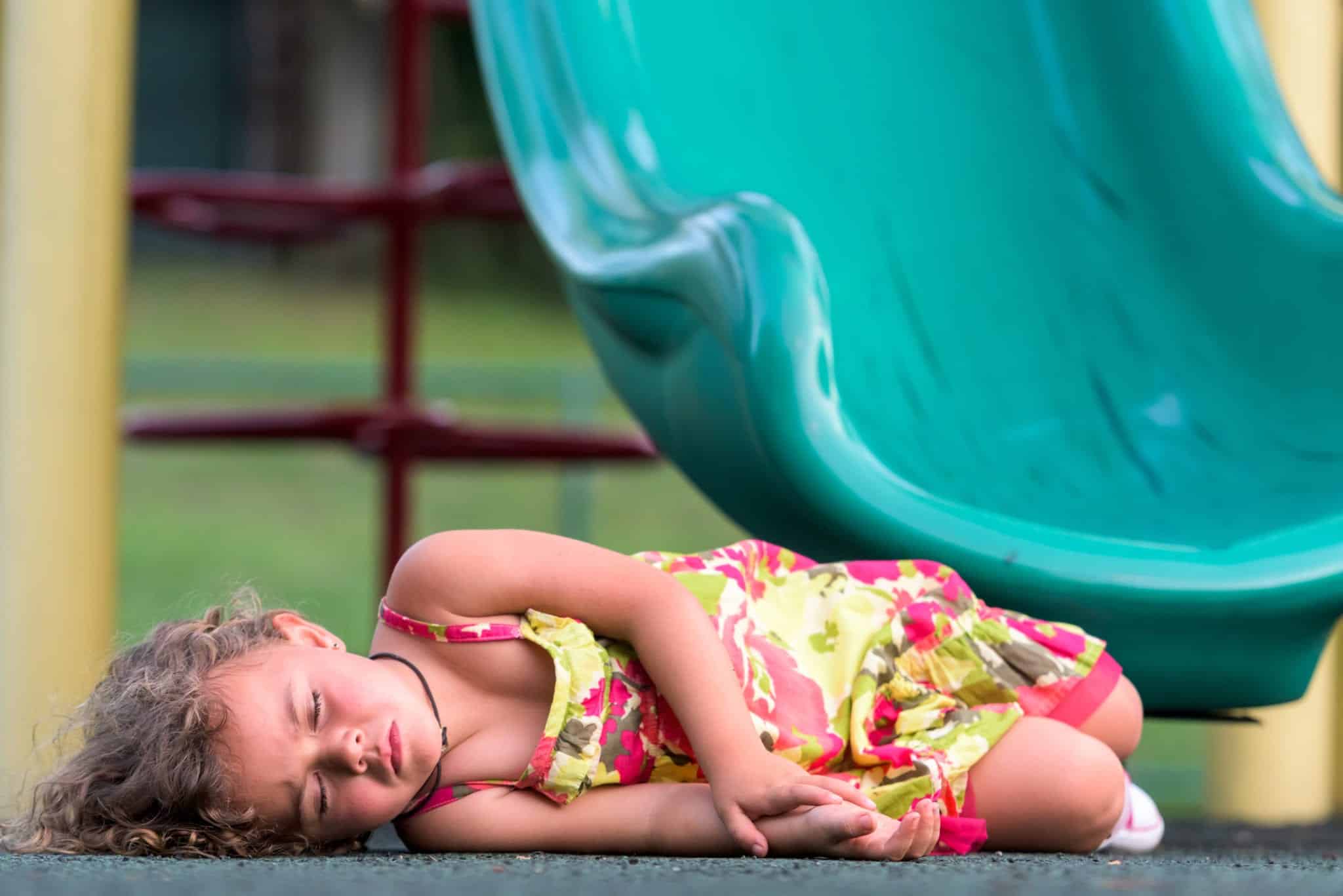 A little girl lying unconscious ground at the bottom of a green slide.