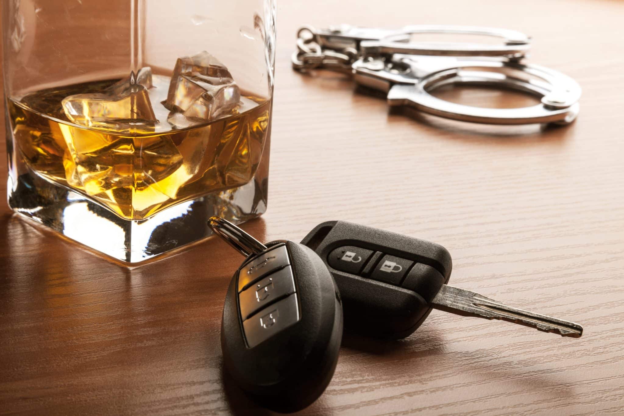 A wooden table with a glass of whiskey, car keys and handcuffs.